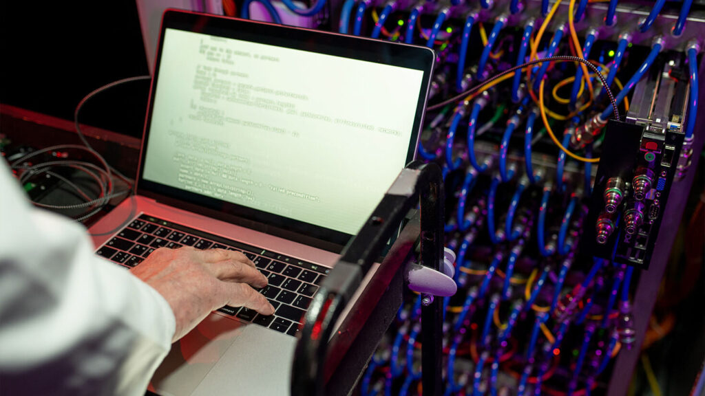 A man with a computer in a server room fixing bugs in a traditional way.